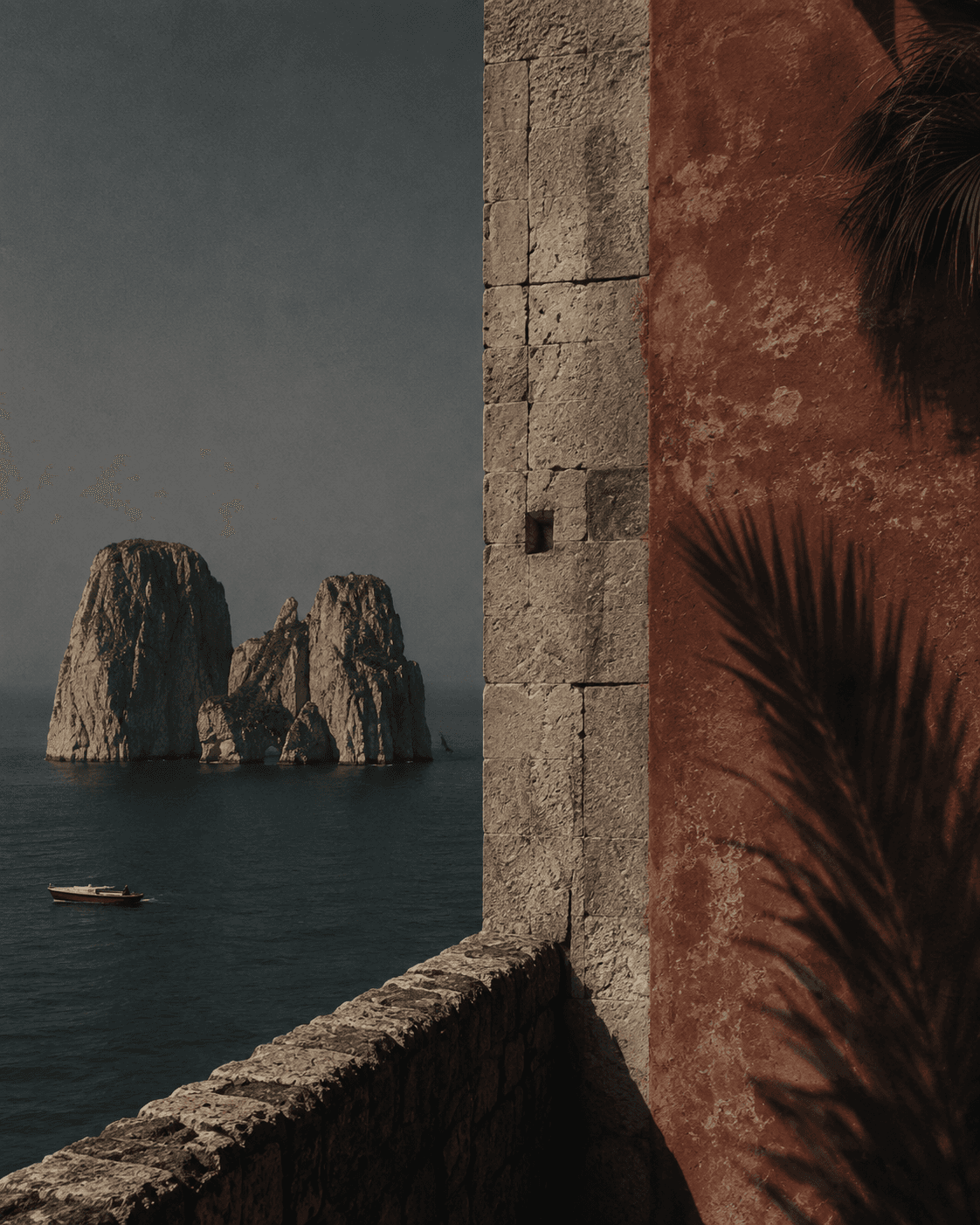 Rock formations in the sea in front of a weathered Mediterranean wall with a palm frond.
