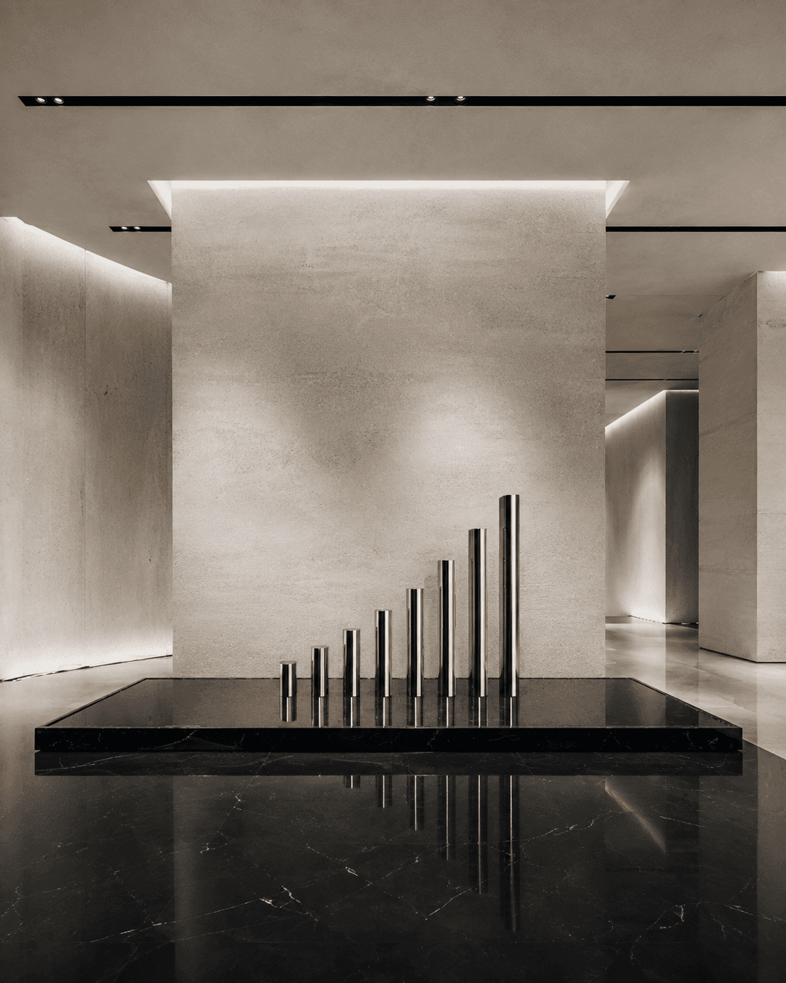 Row of polished chrome cylinders rising in height on a black marble plinth in a stone gallery