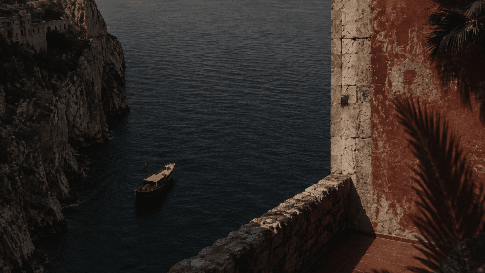 A small boat on dark water below a steep rocky coastline.